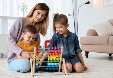 Nanny and little children playing with counting frame at home