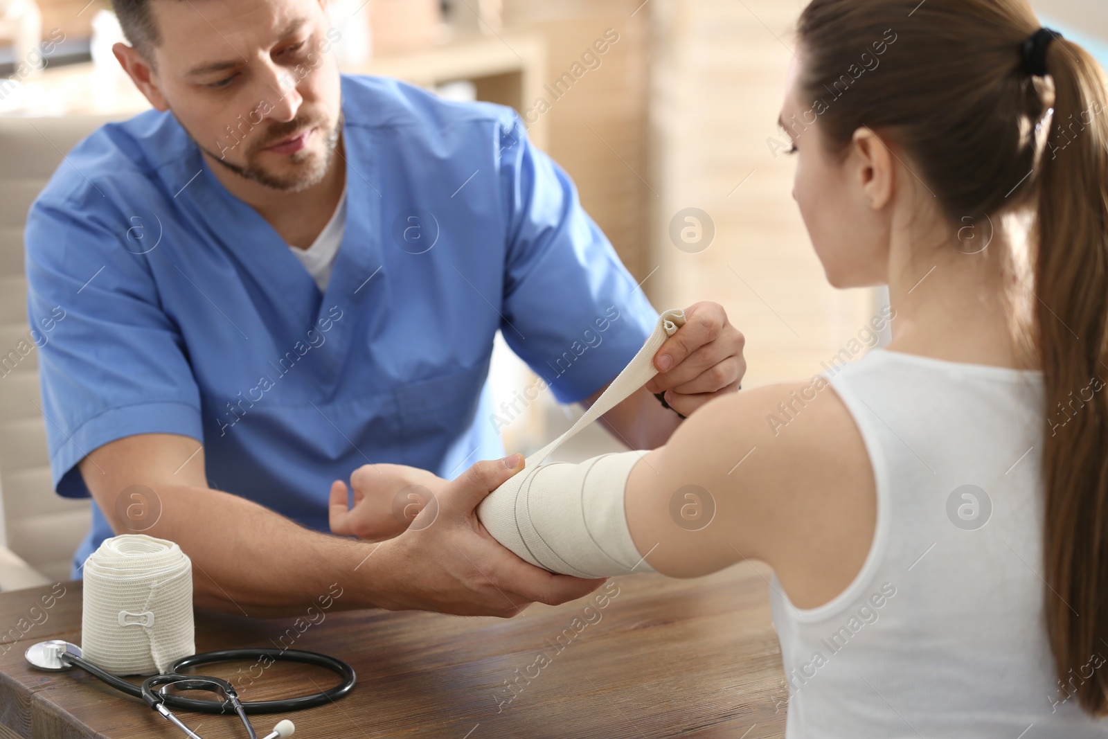 Photo of Male orthopedist applying bandage onto patient's elbow in clinic