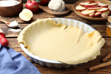 Baking dish with raw dough for apple pie and ingredients on wooden table