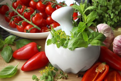 Photo of Mortar with fresh herbs near garlic, pepper and cherry tomatoes on wooden table, closeup
