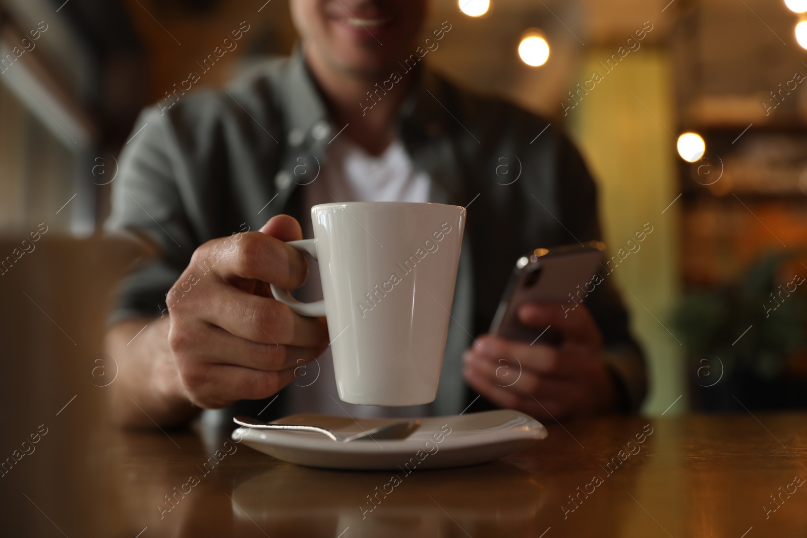 Photo of Man with cup of coffee and smartphone at table in morning, closeup