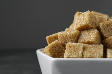 Photo of Brown sugar cubes in bowl on grey background, closeup. Space for text