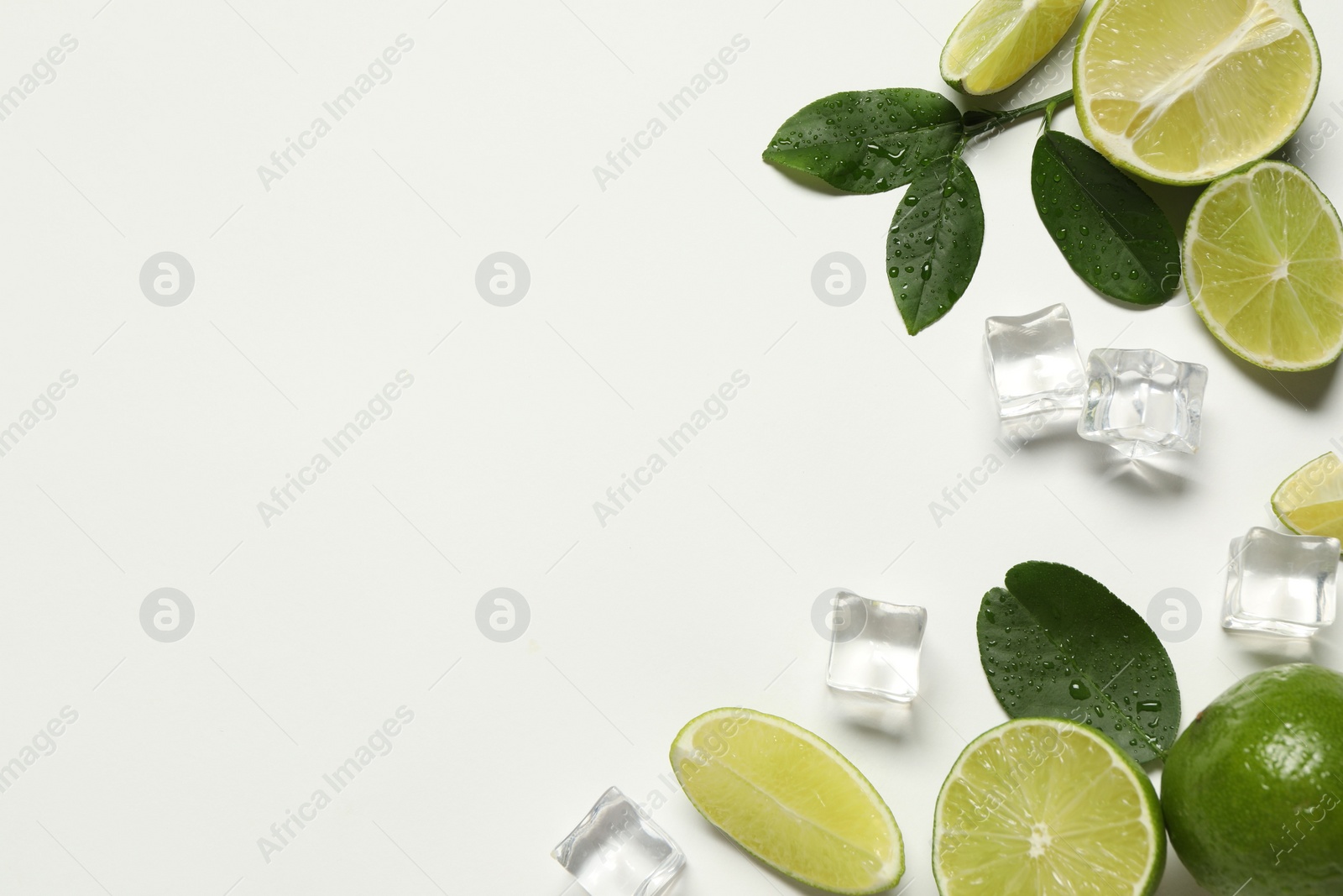 Photo of Fresh ripe limes with green leaves and ice cubes on white background, flat lay