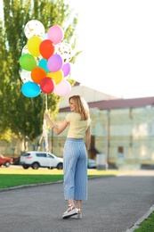 Young woman with colorful balloons outdoors on sunny day