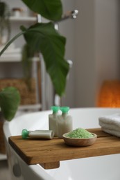 Photo of Wooden tray with cosmetic products and sea salt on bath tub in bathroom, closeup