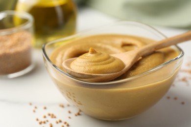 Photo of Spoon and glass bowl with tasty mustard sauce on white table, closeup