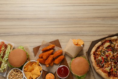 Chicken nuggets, pizza and other fast food on wooden table, flat lay with space for text