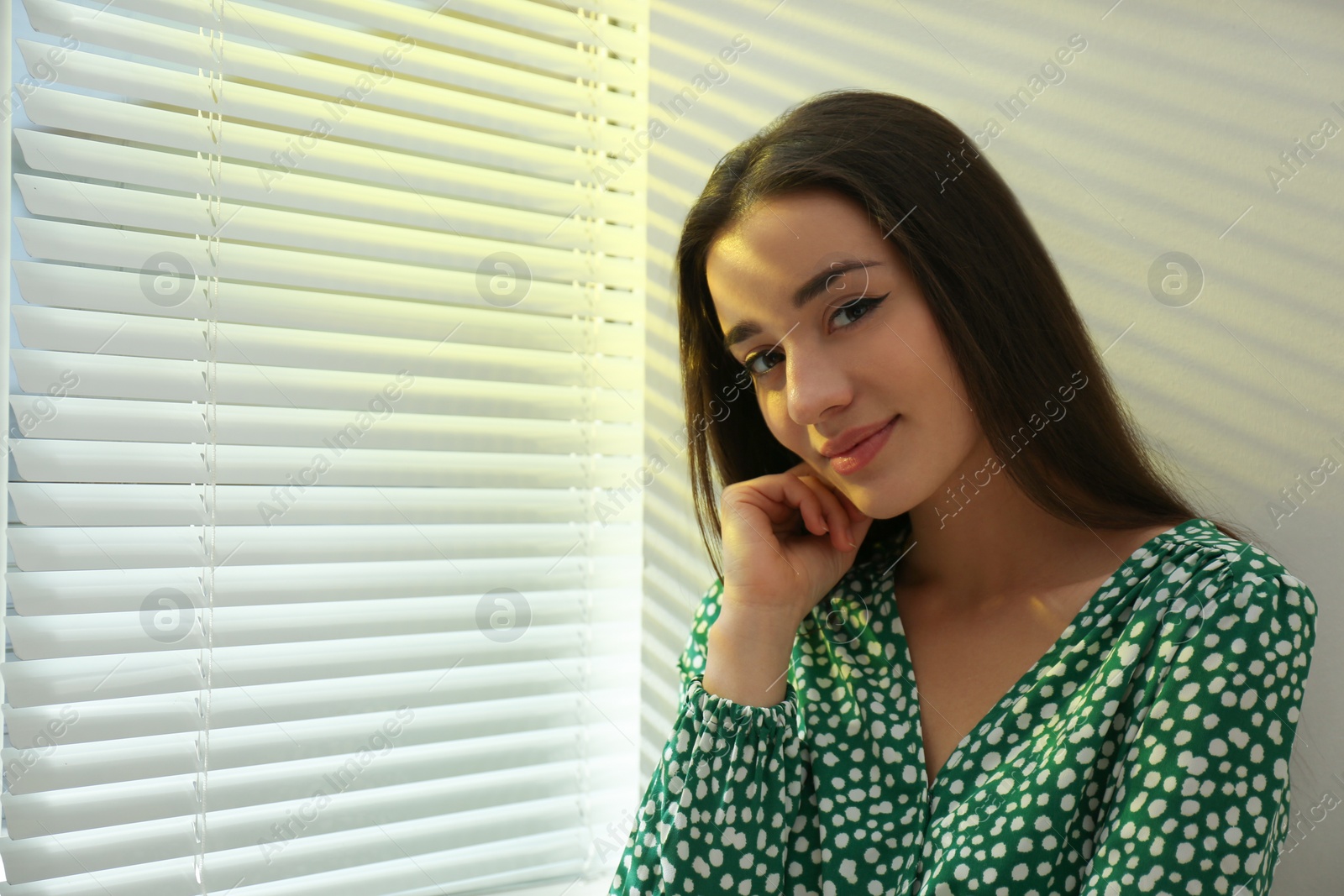 Photo of Young woman near window with Venetian blinds. Space for text