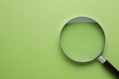 Magnifying glass on green background, top view. Space for text