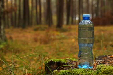 Plastic bottle of fresh water in forest, space for text