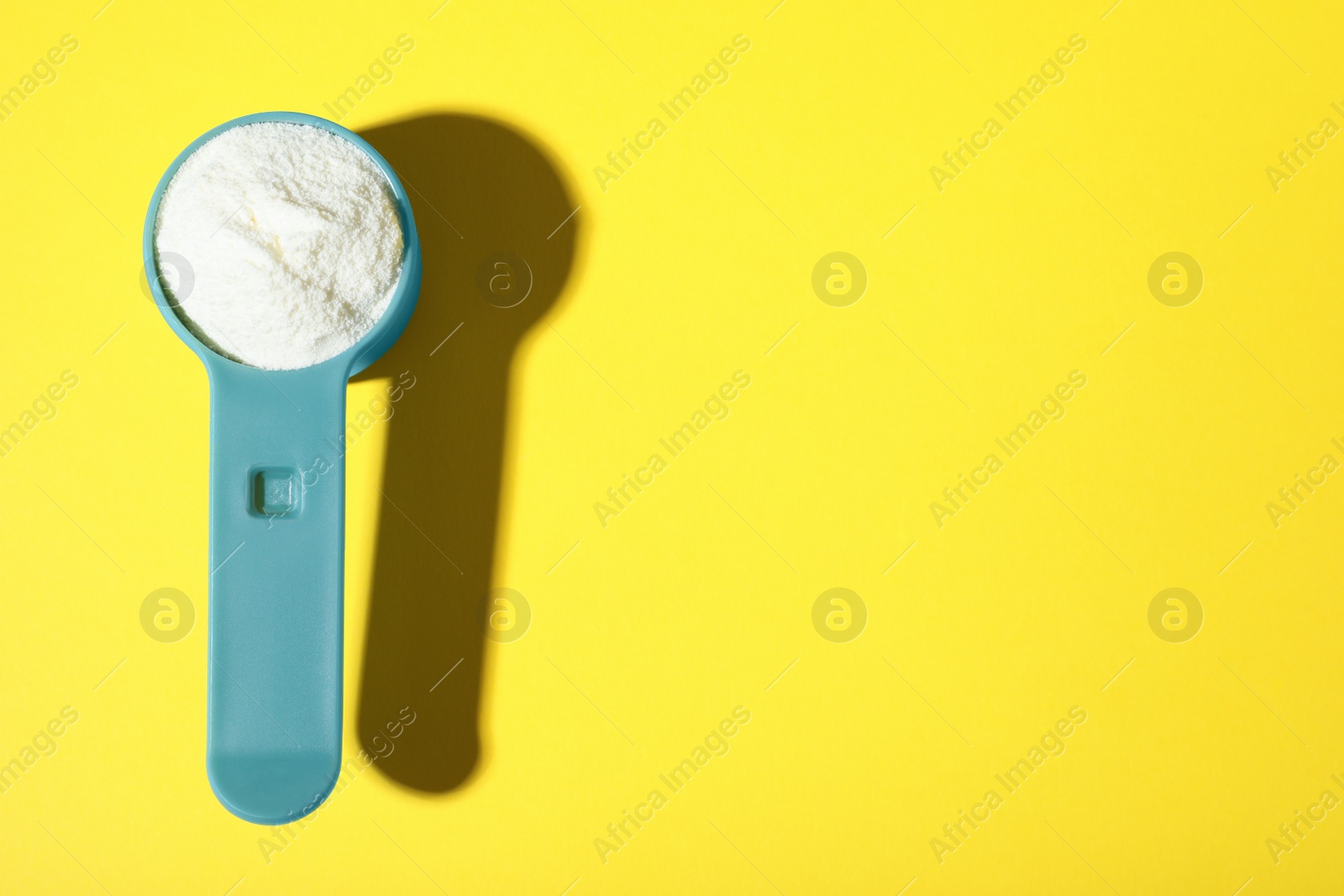 Photo of Scoop of protein powder on yellow background, top view with space for text