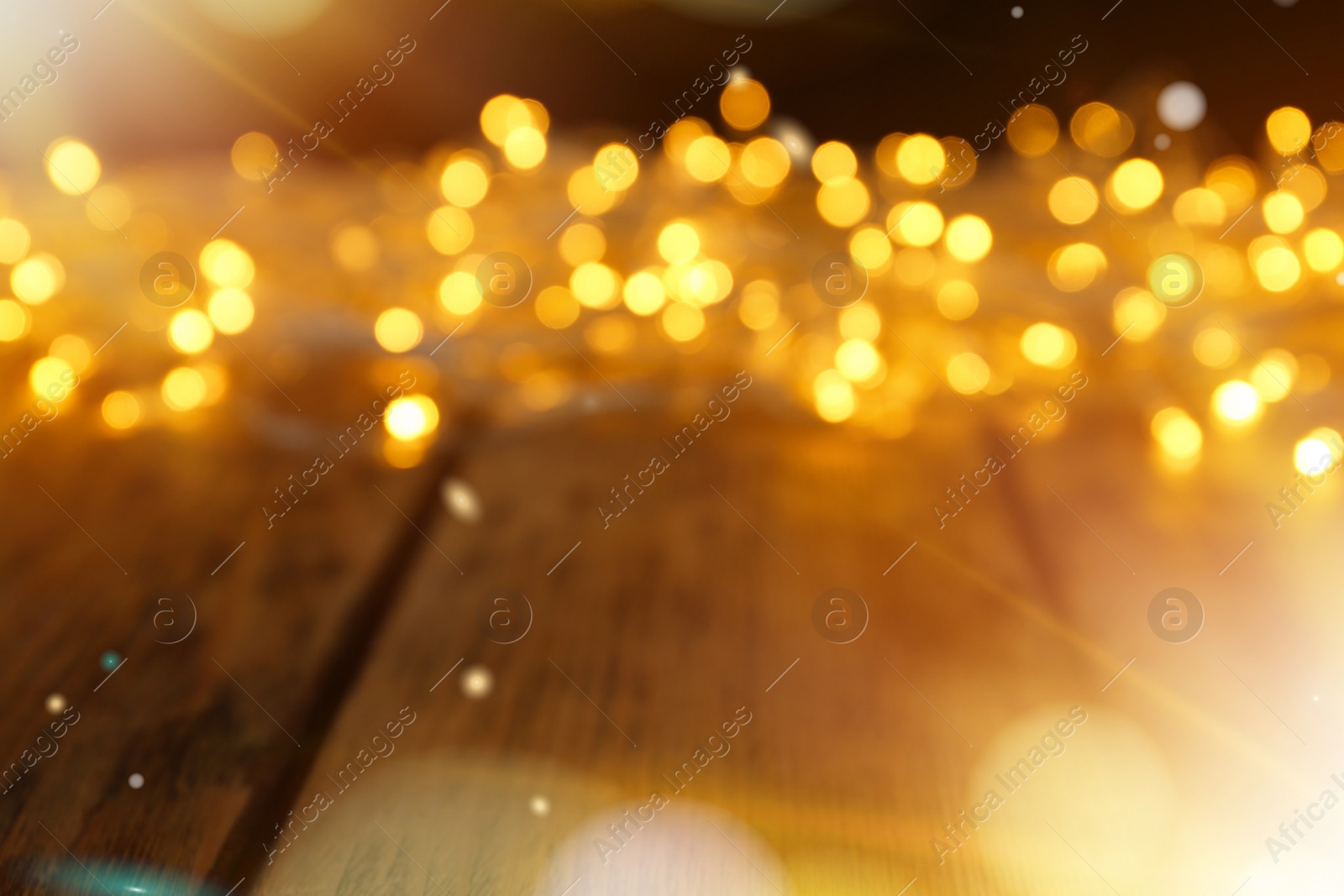 Image of Blurred view of glowing Christmas lights on wooden table