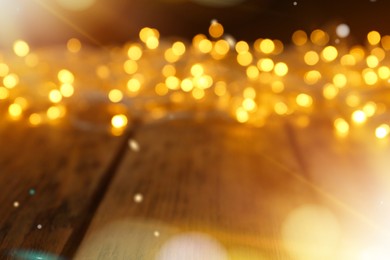 Blurred view of glowing Christmas lights on wooden table