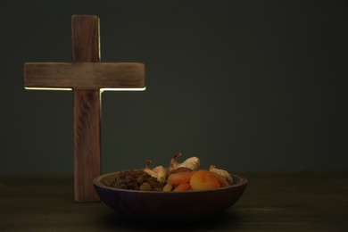 Photo of Cross and dried fruits on wooden table, space for text. Lent season