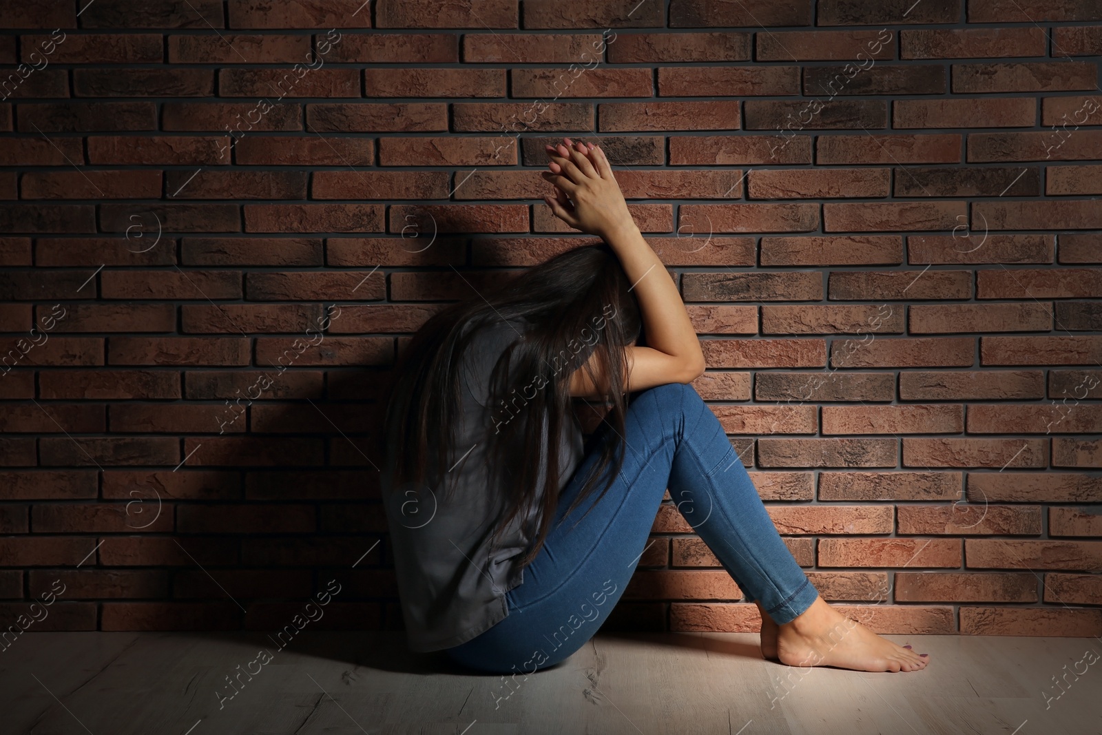 Photo of Depressed young woman sitting on floor near brick wall