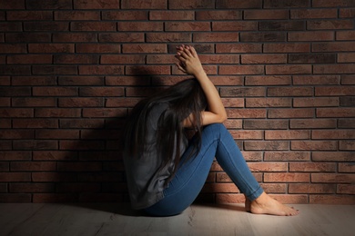 Depressed young woman sitting on floor near brick wall