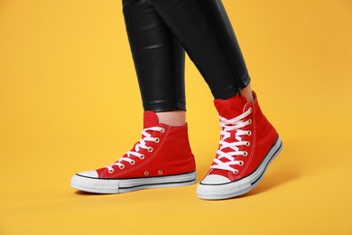 Photo of Woman wearing pair of new stylish sneakers on yellow background, closeup