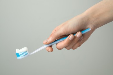 Woman holding toothbrush with paste on light grey background, closeup