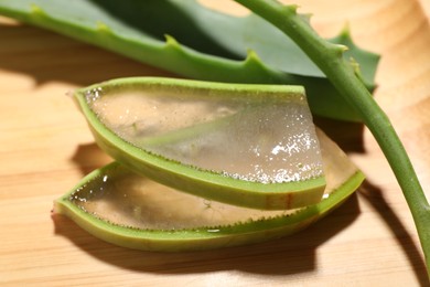 Photo of Slices of fresh aloe vera leaves with gel on wooden table, closeup
