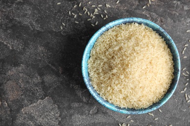 Photo of Bowl with uncooked rice on grey background, top view. Space for text