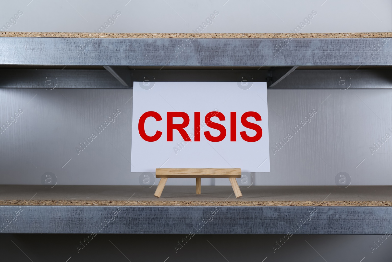 Photo of Wooden easel with word Crisis on canvas at shelf