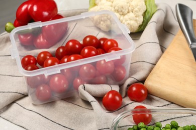 Photo of Container with tomatoes and fresh products on table, closeup. Food storage