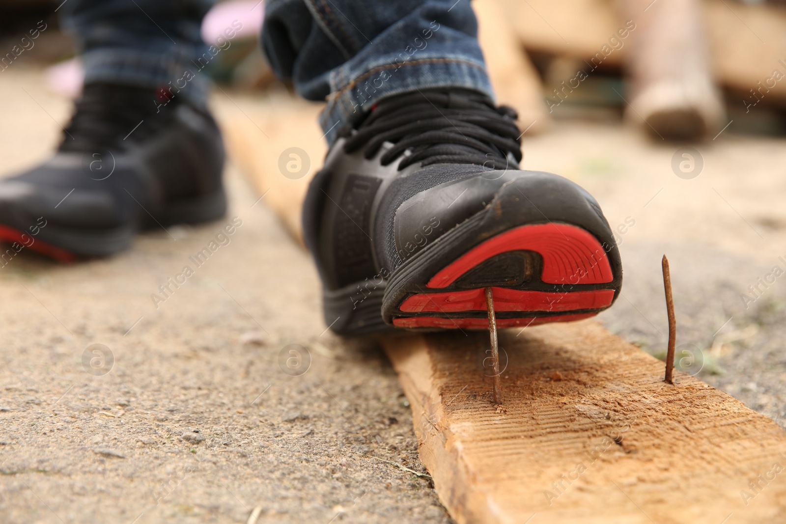 Photo of Careless worker stepping on nail in wooden plank outdoors, closeup