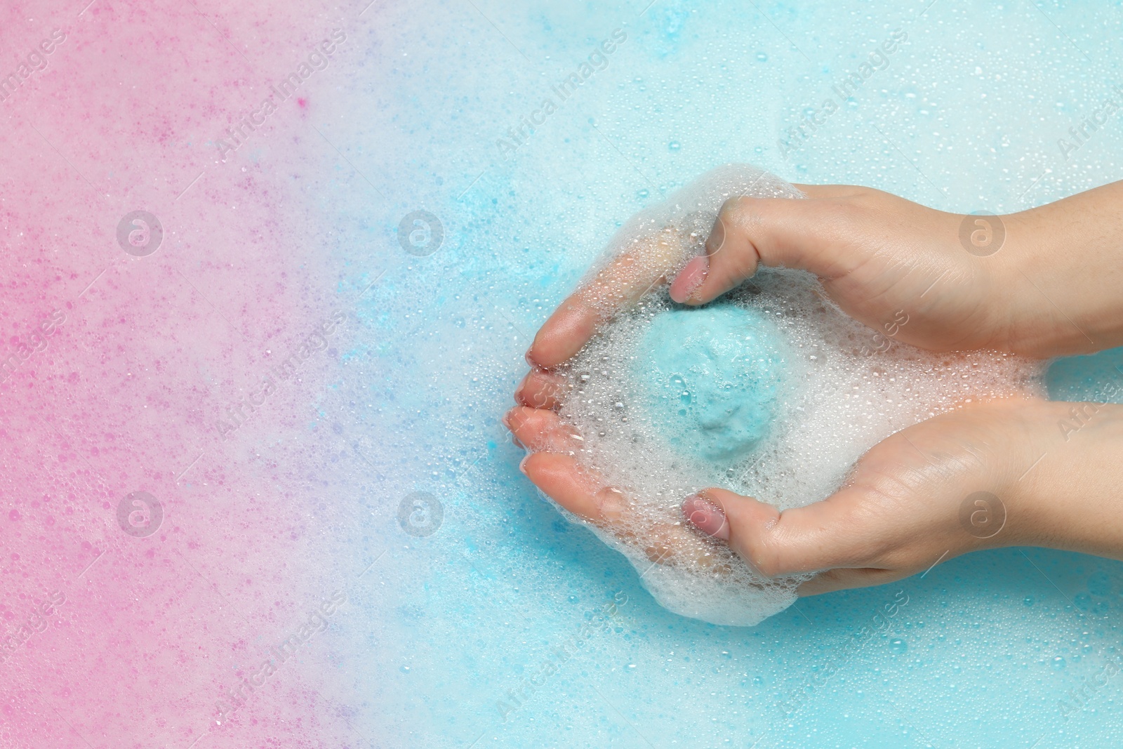 Photo of Woman holding bath bomb over water with foam, top view. Space for text