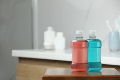 Bottles with mouthwash on wooden table in bathroom, space for text