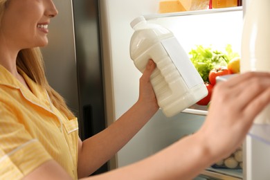 Young woman putting gallon of milk into refrigerator indoors, closeup