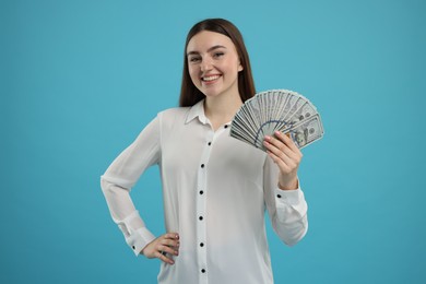 Happy woman with dollar banknotes on light blue background