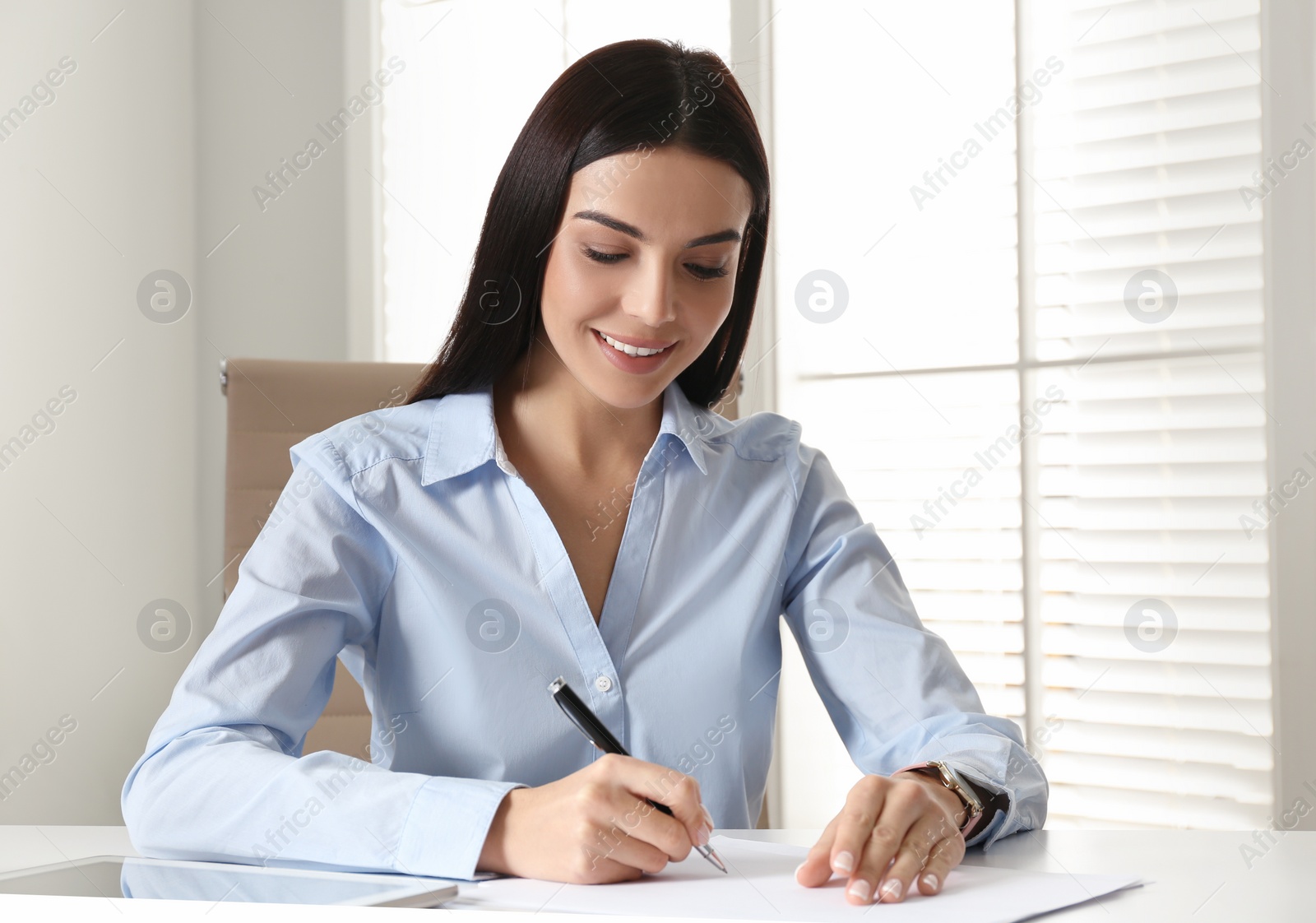 Photo of Young businesswoman writing at table in office