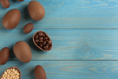 Photo of Sweet chocolate eggs and candies on light blue wooden table, flat lay. Space for text