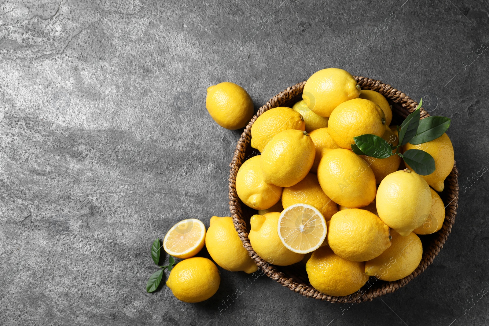 Photo of Fresh lemons in wicker basket on grey table, top view. Space for text