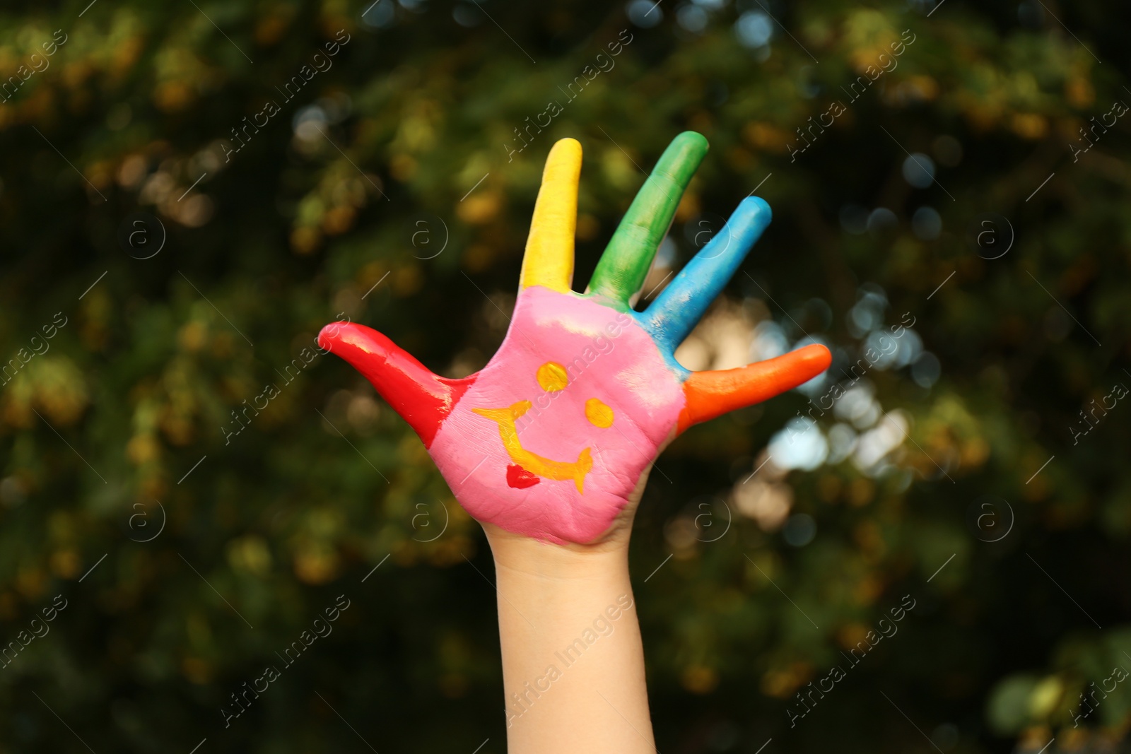 Photo of Kid with smiling face drawn on palm in green park, closeup. School holidays