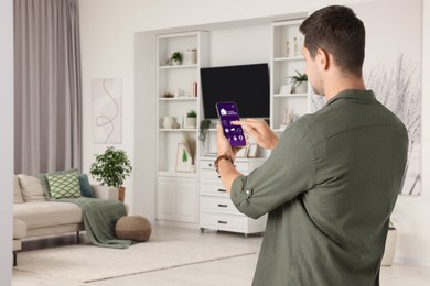 Man using smart home control system via application on mobile phone indoors