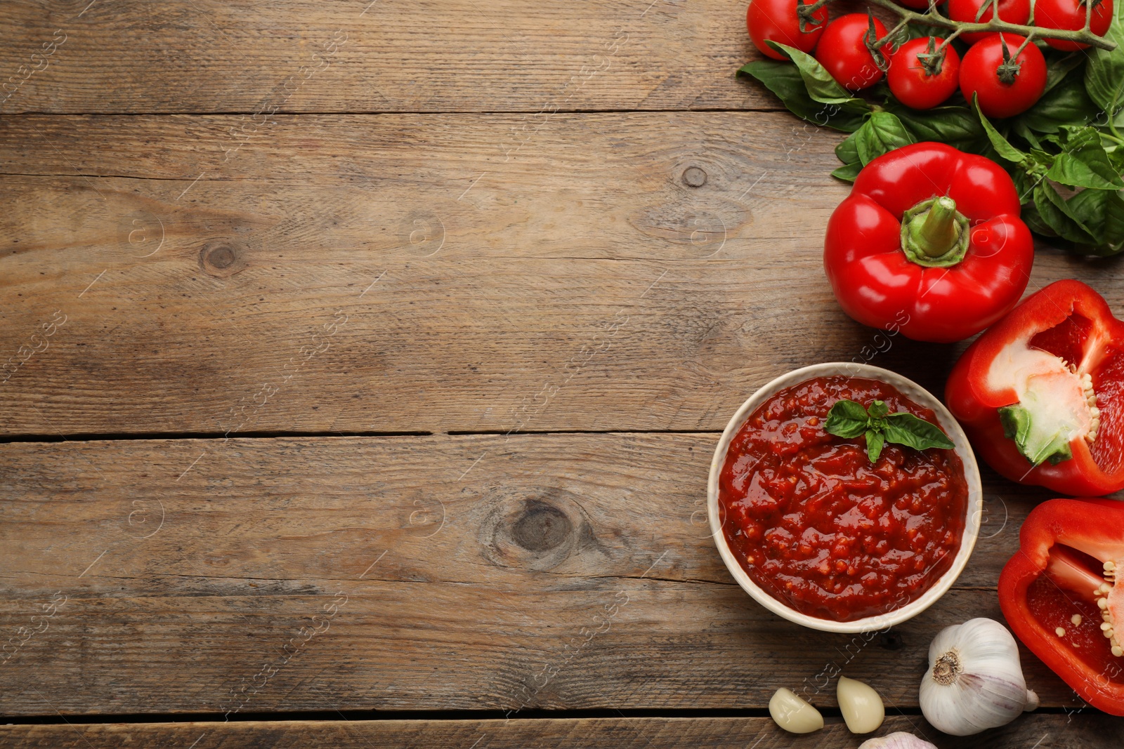 Photo of Delicious adjika sauce in bowl and ingredients on wooden table, flat lay. Space for text