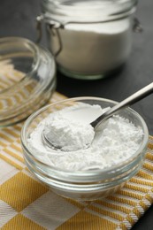 Photo of Baking powder in bowl, jar and spoon on black table, closeup