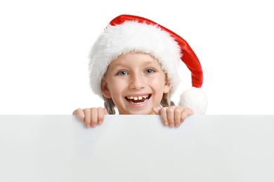 Photo of Happy child in Santa hat peeping out of blank banner on white background. Christmas celebration