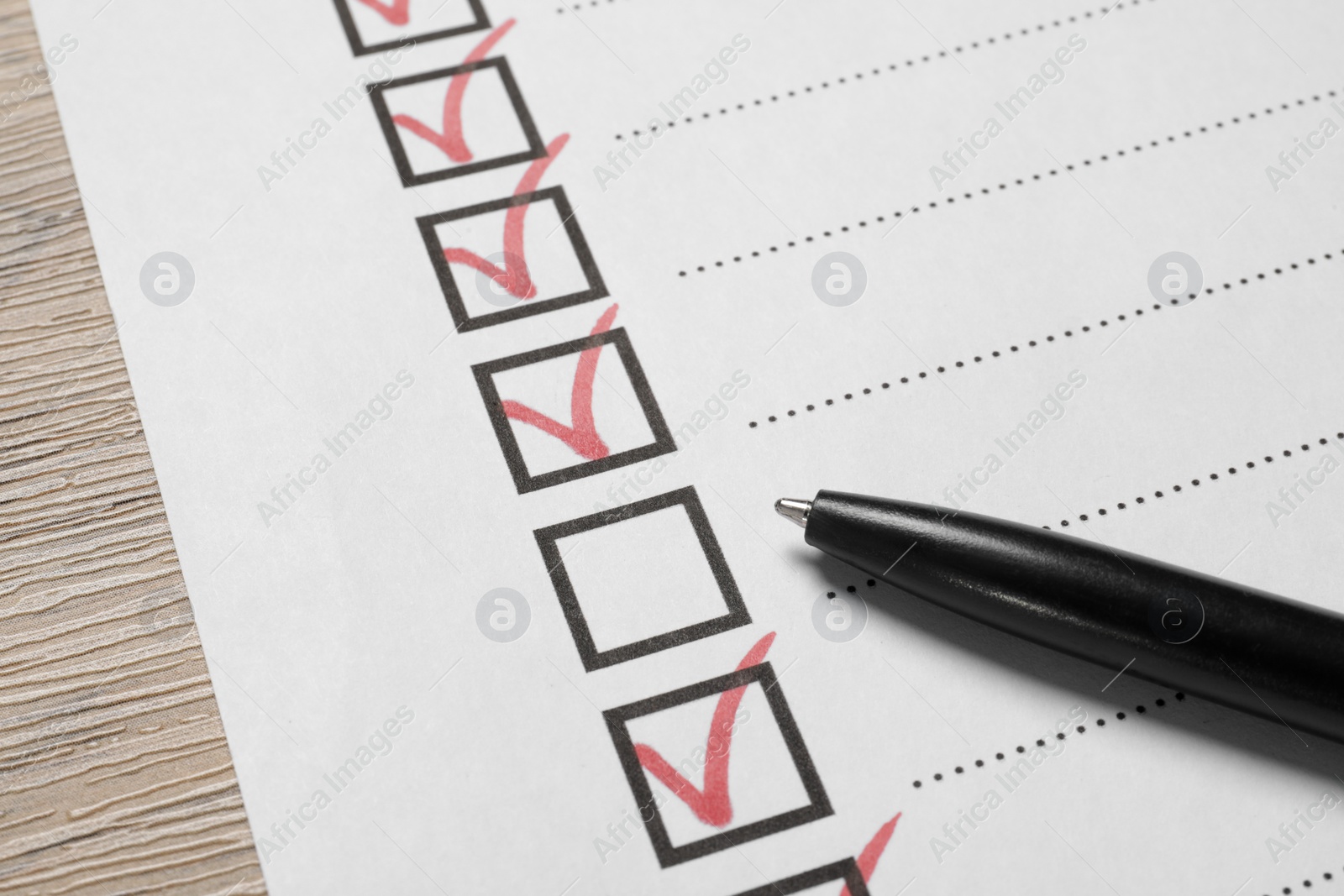 Photo of Paper sheet with checkboxes and pen on wooden table, closeup. Checklist