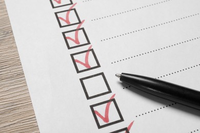 Photo of Paper sheet with checkboxes and pen on wooden table, closeup. Checklist