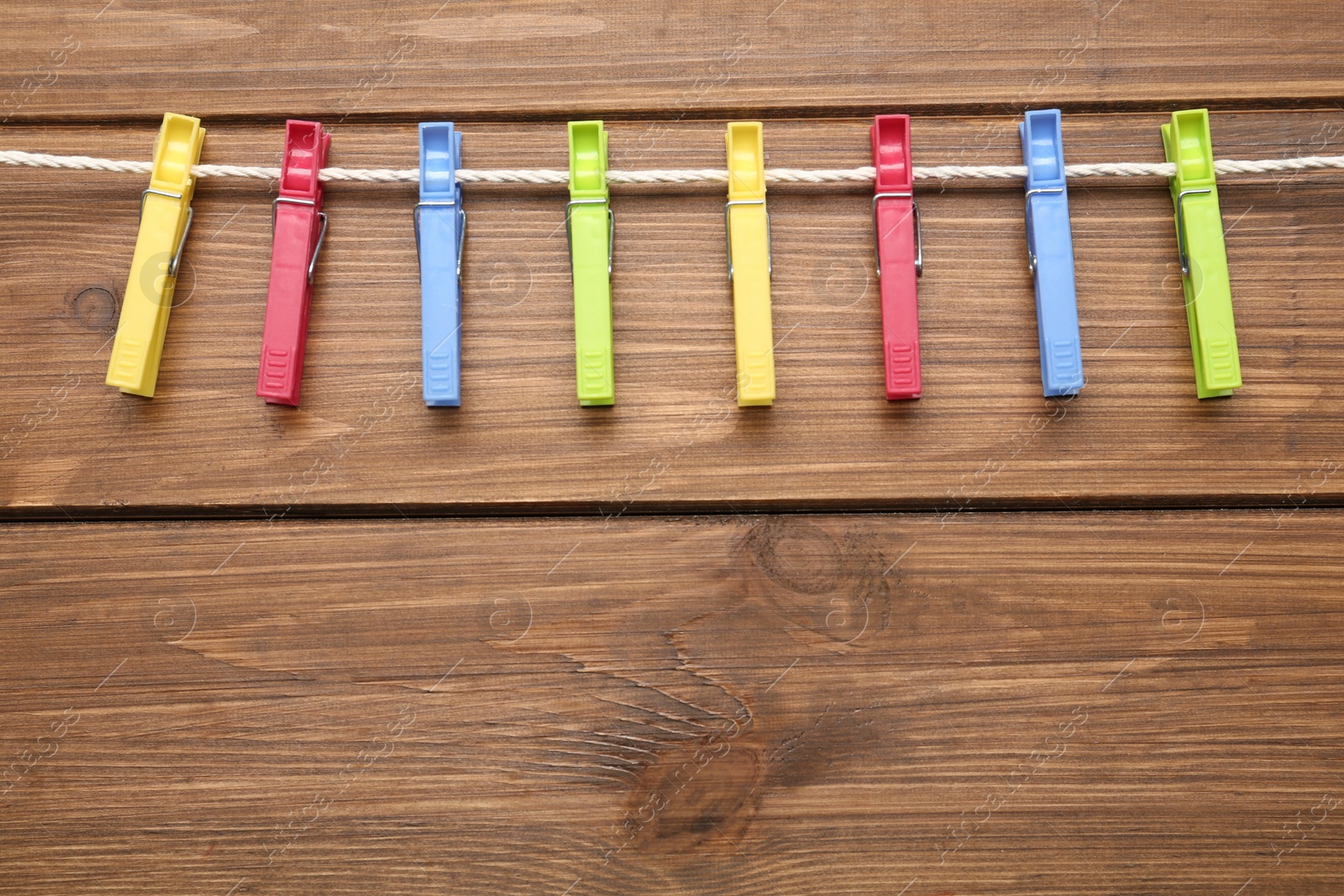 Photo of Colorful plastic clothespins and rope on wooden background. Space for text