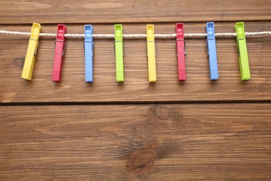 Colorful plastic clothespins and rope on wooden background. Space for text