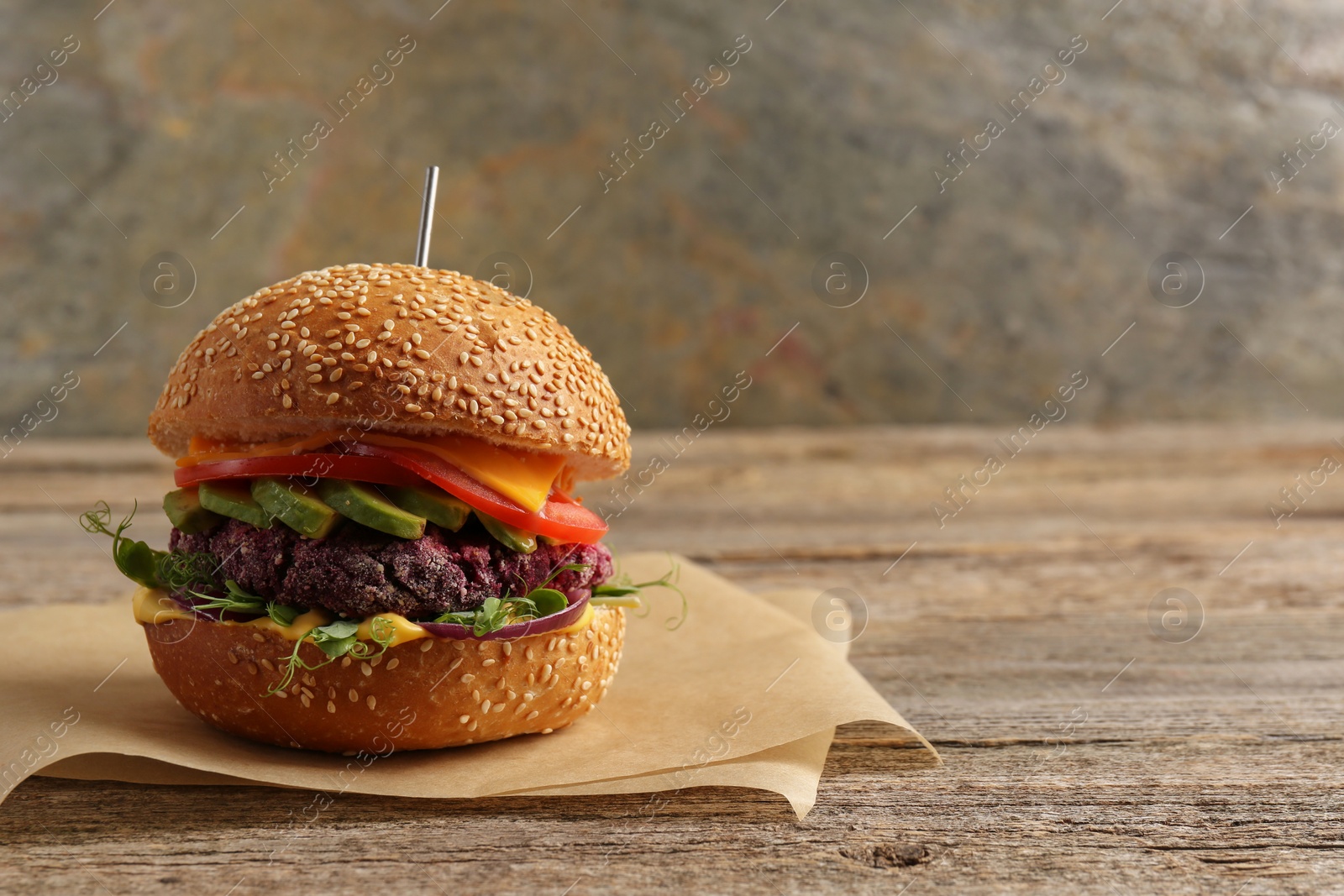 Photo of Tasty vegetarian burger with beet cutlet, cheese, avocado and tomato on wooden table, space for text