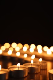 Photo of Burning candles on dark surface against black background, closeup. Space for text