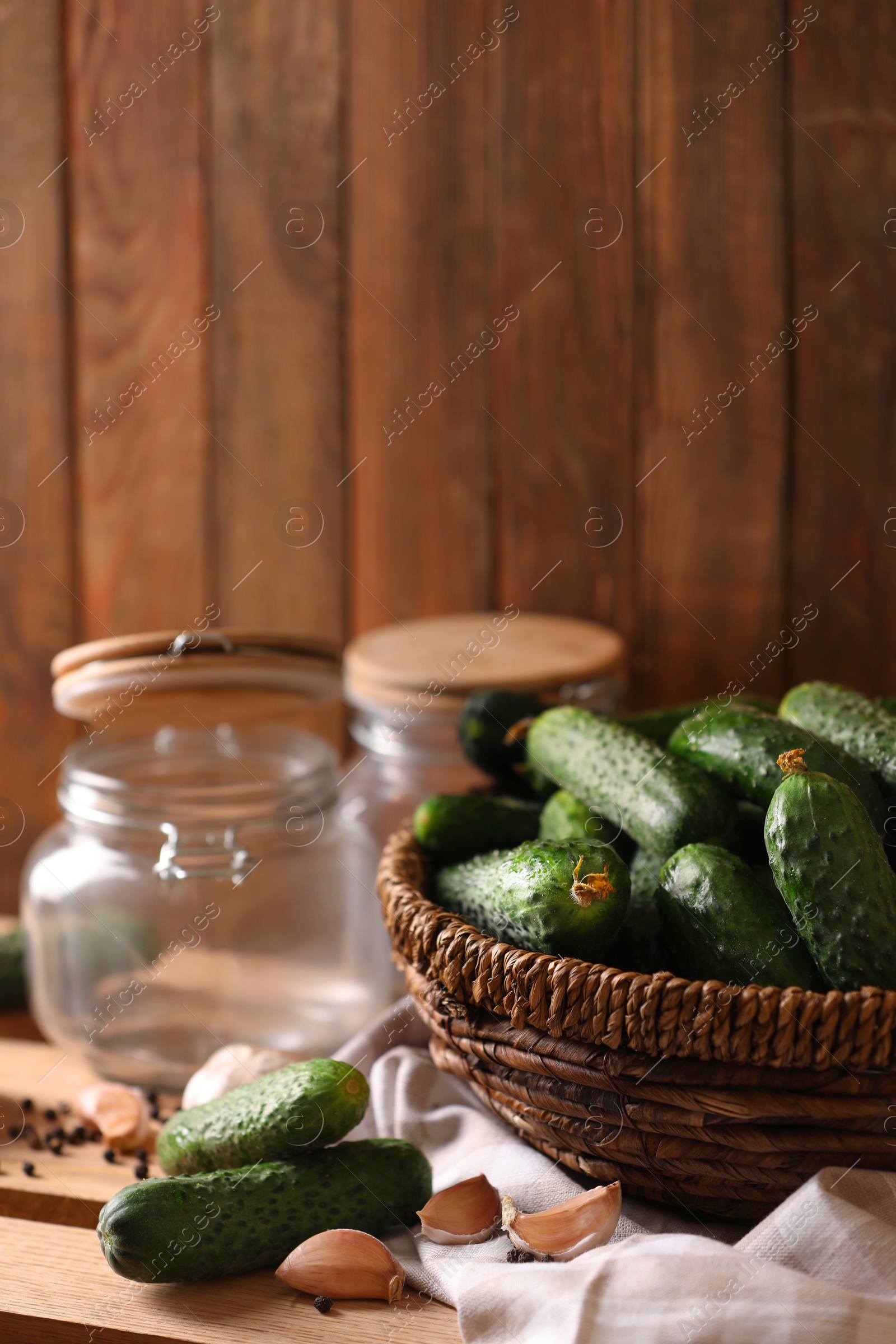 Photo of Fresh cucumbers and other ingredients near empty jars prepared for canning on wooden table