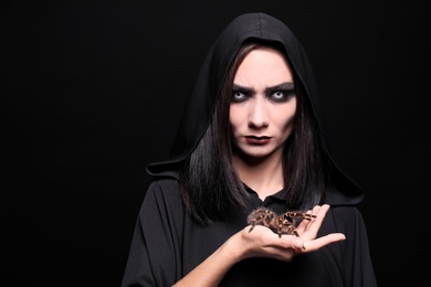 Photo of Mysterious witch with spooky spider on black background, space for text