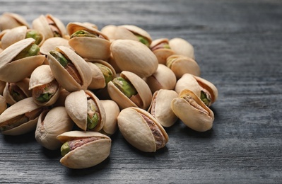 Photo of Heap of organic pistachio nuts on wooden table, closeup