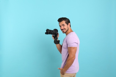 Young photographer with professional camera on light blue background. Space for text