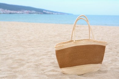 Photo of Stylish straw bag on sand near sea, space for text. Beach accessory